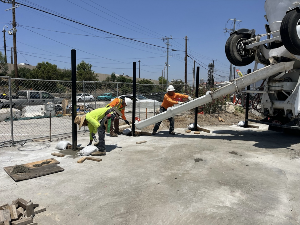 Three construction workers in bright safety gear direct wet concrete from a mixer onto a construction site.