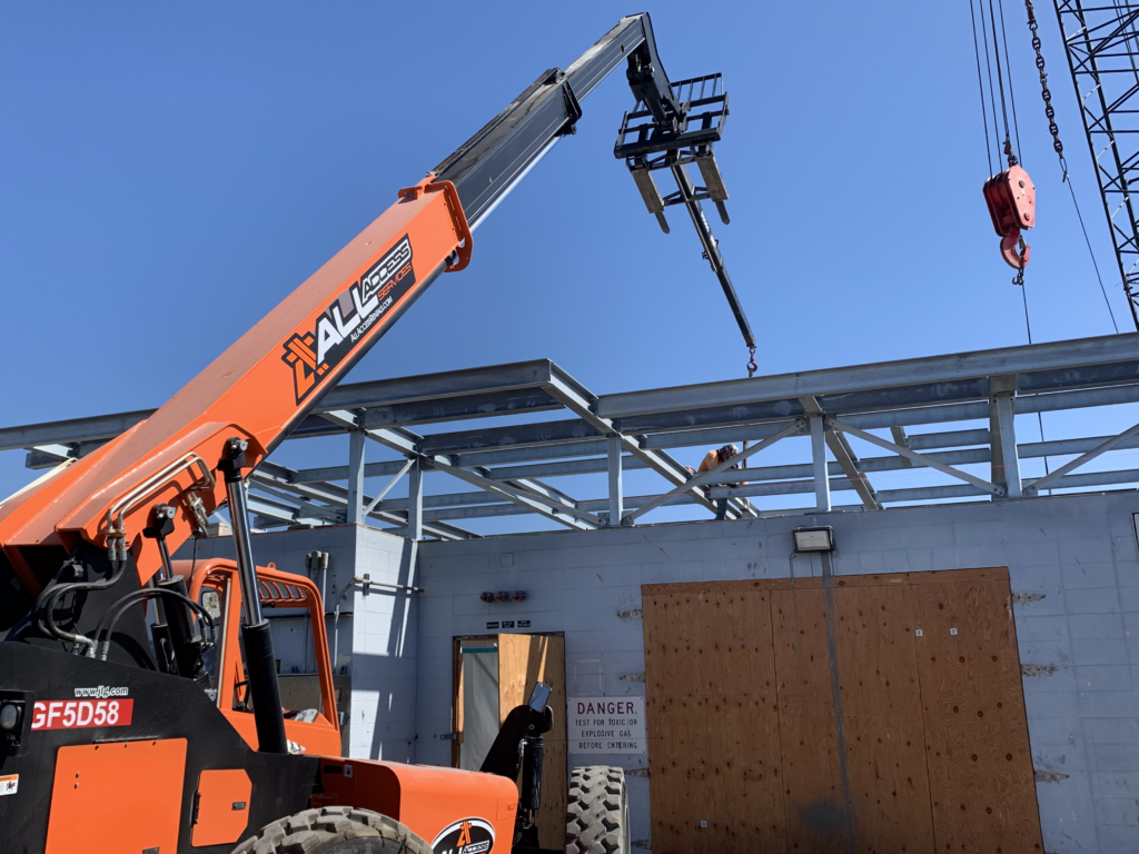 Construction site with an orange telescopic boom lift and a partially constructed roof framework