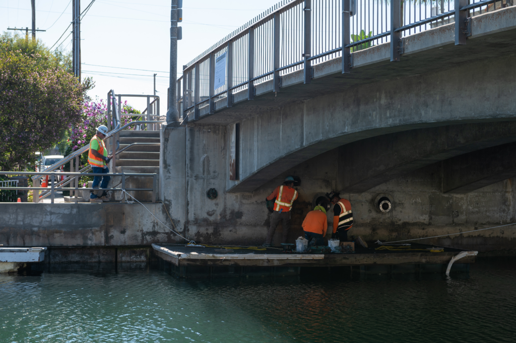 Alamitos Bay - workers under a bridge working from a platform - frontal view