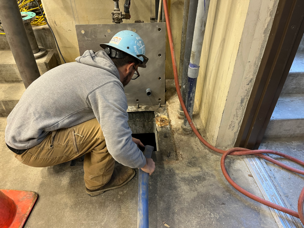 A worker in hardhat working with a flexible tube within a hatch.
