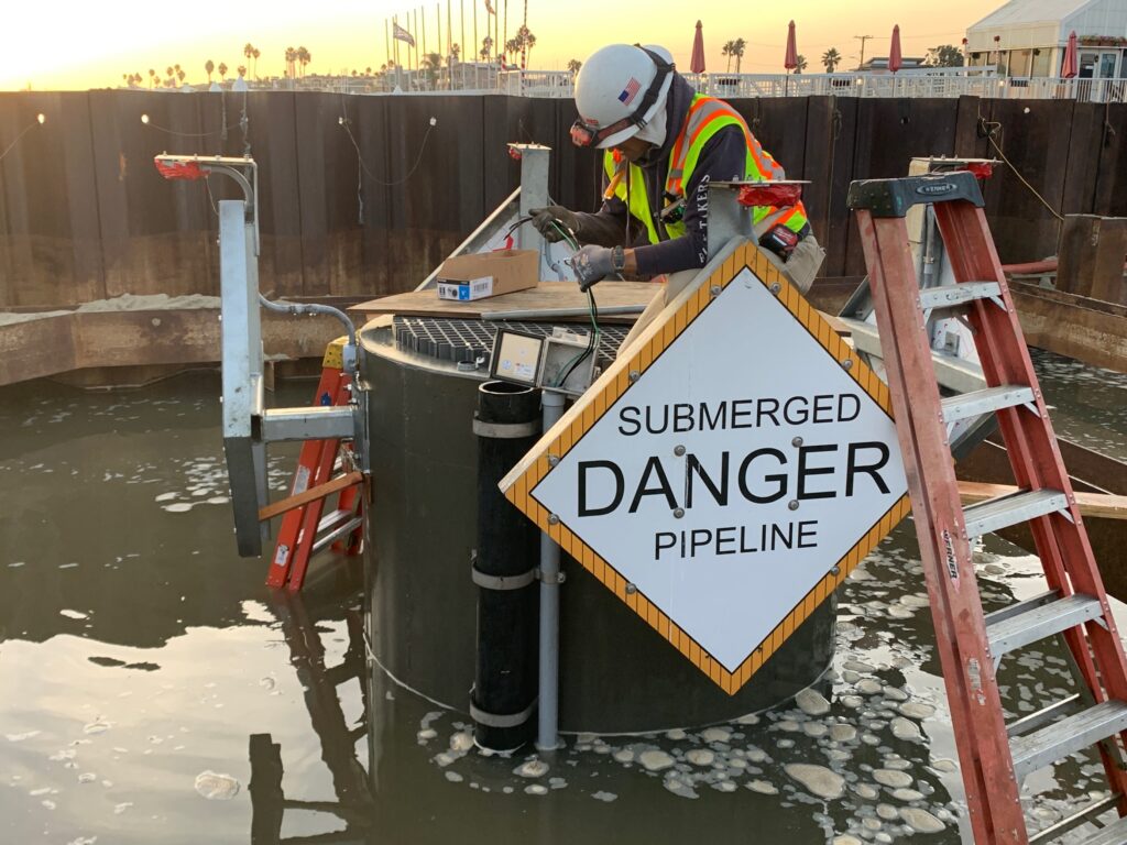 A technician works on the wiring of a submerged pipeline at Alamitos Bay Pump Station, with water all around.